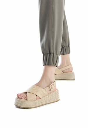 Las sandalias de plataforma beiges tejidas presentan un diseño entrecruzado, correa para el tobillo ajustable y suelas texturizadas al estilo de alpargatas.
