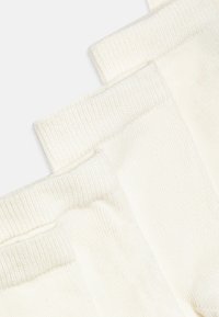 Chaussettes en coton blanc avec des bords côtelés, présentant une texture douce et une finition lisse, disposées en position empilée.