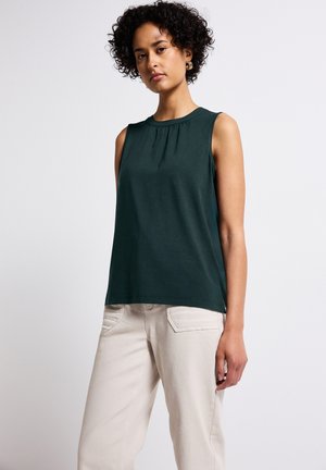 Haut sans manches vert foncé en tissu doux, avec un col plissé et une coupe décontractée, associé à un pantalon beige clair.