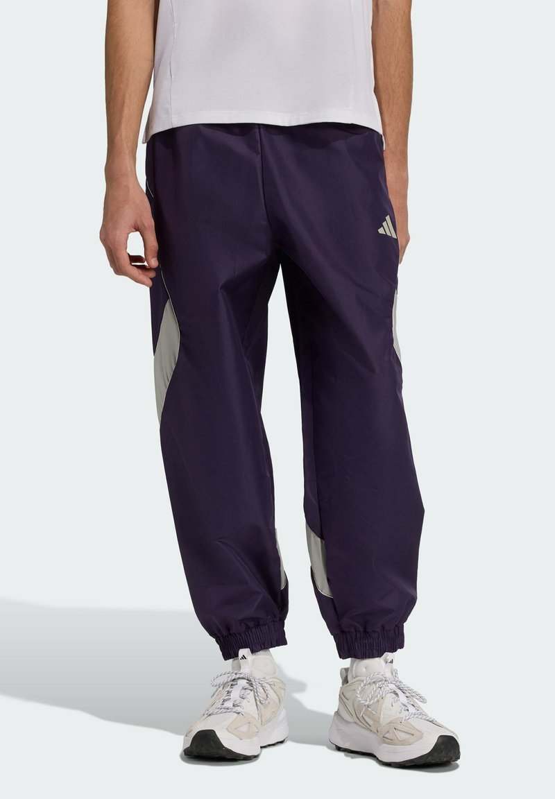 Fialové športové nohavice s elastickými manžetami, s striebristými bočnými panelmi a logom Adidas. Vyrobené z ľahkej, hladkej látky.