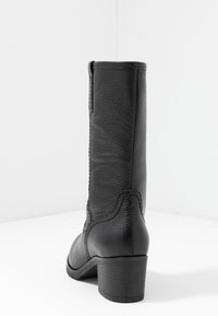 Botas de cuero negro con un acabado texturizado, que cuentan con un tacón medio y un diseño elegante y erguido. Sin herrajes visibles ni detalles adicionales.