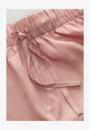 Pink satin shorts feature an elastic waistband with a drawstring tie, smooth texture, and subtle heart patterns throughout.