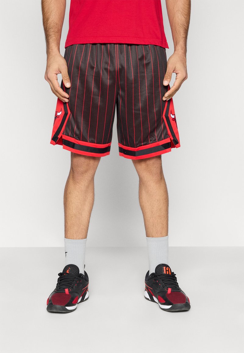 Μαύρα σορτς μπάσκετ με κόκκινες ρίγες, διαθέτουν λογότυπο στο πλάι και κόκκινες λεπτομέρειες. Συνδυάζονται με αθλητικά παπούτσια σε μαύρο και κόκκινο και γκρι κάλτσες.