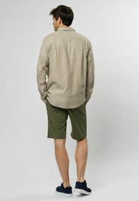 Lichtbeige lange mouwen shirt met knoopdetails, gecombineerd met olijfgroene shorts. Schoenen zijn marineblauwe sneakers. Eenvoudige, casual outfit.