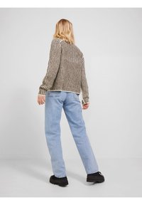 Chunky, brun og kremstripet strikkegenser med løs passform. Lyseblå, rettskårne jeans og svarte platåsko fullfører antrekket.