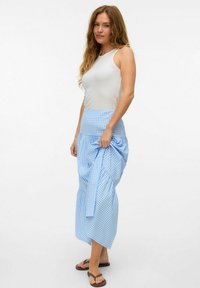 Ljusblå rutiga maxikjol med hög midja, rynkat mönster och lätt glans; tillsammans med en tajt vit linne och flip-flops.