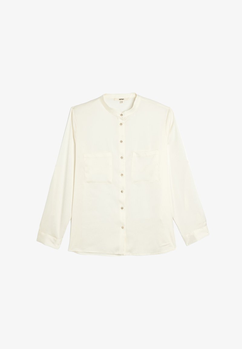 White long-sleeve shirt with a rounded collar, front button closure, and two chest pockets. Soft fabric with a smooth texture.
