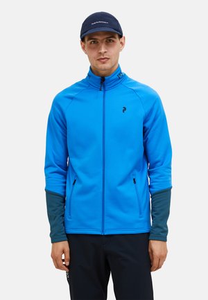 Blaues Sportjacke mit hohem Kragen, Reißverschluss vorne und kontrastierenden dunkelgrünen Bündchen. Verfügt über seitliche Reißverschlusstaschen und ein Logodetail auf der Brust.