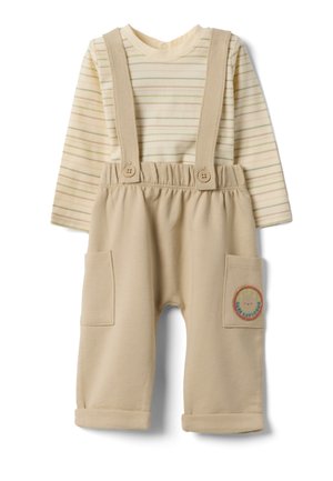Beige Baby-Latzhosen mit umgeschlagenen Bündchen und aufgesetzten Taschen, kombiniert mit einem langärmligen Cremehemd mit dünnen beigen Streifen.