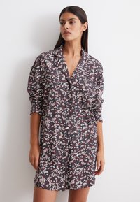 Vestito camicia floreale con uno sfondo scuro e fiori rosa e bianchi, chiusura frontale con bottoni, colletto e maniche lunghe.