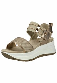 Béžové sandály s texturovaným kovovým páskem, dvěma elastickými pásky a bílou polstrovanou podrážkou. Mají plochý podpatek a měkké vnitřní podšívku.