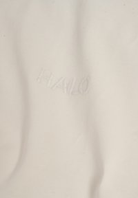 Biała tkanina o gładkiej fakturze z wyhaftowanym słowem "HALO" w lekko podniesionej, subtelnej czcionce.