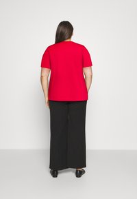 T-shirt corto rosso a maniche corte, tessuto morbido, scollatura rotonda, abbinato a pantaloni neri a gamba larga, texture liscia, e scarpe basse.
