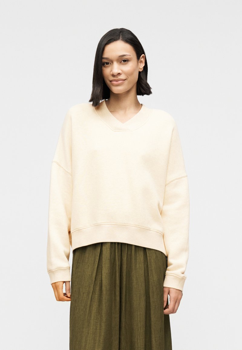 Sweat-shirt ample beige clair avec col en V, épaules tombantes et poignets côtelés, associé à une jupe texturée vert olive.