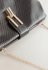 Sort faux python clutch med en tekstureret overflade, der har en klips i guldfarvet og en gylden kædestrop, der er fastgjort i siderne.