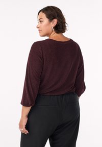 Burgundská, textúrovaná blúzka s voľným strihom, trojštvrťové rukávy a okrúhly výstrih, v kombinácii s čiernymi nohavicami s zadnými vreckami.