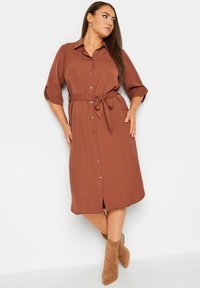 Braunes Hemdkleid mit tailliertem Gürtel, dreiviertellangen Ärmeln und leicht ausgestellt Rock. Es hat vordere Knöpfe und eine glatte Textur.