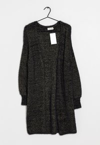 Černý a zlatý huňatý pletený kardigan s dlouhými rukávy a otevřeným předním dílem, zavěšený na černém ramínku na bílém pozadí.