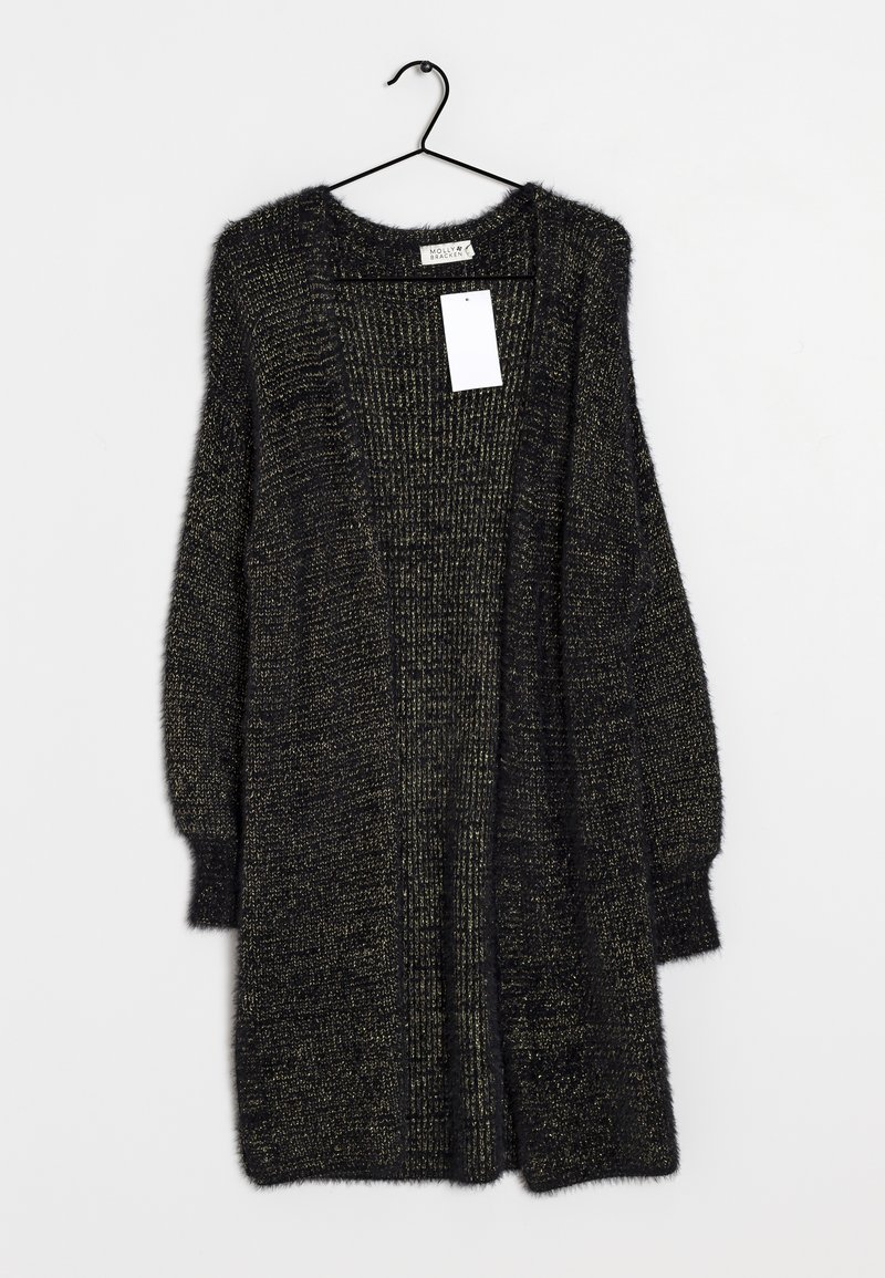 Černý a zlatý huňatý pletený kardigan s dlouhými rukávy a otevřeným předním dílem, zavěšený na černém ramínku na bílém pozadí.