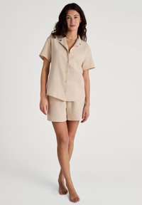 Beige set met korte mouwen en bijpassende shorts, gemaakt van een gestructureerde stof, met een knoopsluiting aan de voorkant en een ontspannen pasvorm.