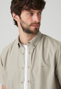 Light beige short-sleeve button-up shirt with a soft texture, featuring a small logo, classic collar, and light brown buttons.