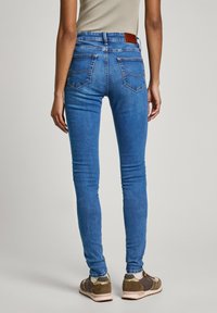 Jeans skinny de mezclilla azul con una cintura de altura media, que presentan bolsillos traseros sutiles y un parche de cuero marrón en la cinturilla. Tejido texturizado.