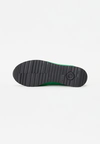 Semelle en caoutchouc noir d’une chaussure verte avec des rainures horizontales profondes et un motif circulaire près du talon, marquée Gabor au centre de la semelle.