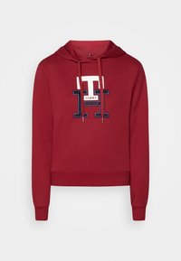 Sudadera roja con un logo frontal que presenta "TOMMY HILFIGER". Tiene capucha con cordón, puños de canalé y un diseño recortado. Textura suave de algodón.