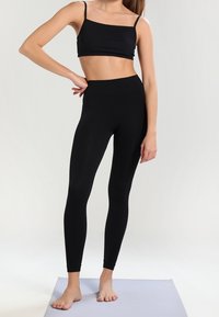 Top corto nero con spalline sottili, abbinato a leggings neri a vita alta. Tessuto liscio ed elasticizzato con un design aderente.