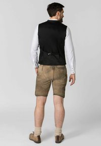 Eine schwarze Weste mit glatter Textur, getragen über einem weißen Langarmhemd, kombiniert mit braunen Ledershorts und hellbraunen Schuhen.