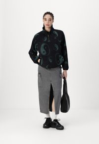 Fekete gyapjú pulóver zöld yin-yang mintákkal, fél cipzáros kivitel. Szürke farmer szoknya elöl hasítékkal, fekete sportcipővel és fekete táskával párosítva.