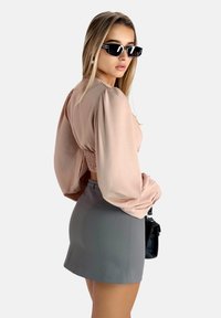 Geflochtene beige Bluse mit gepufften Ärmeln, kombiniert mit einem taillierten grauen Minirock. Eine schwarze Handtasche und Katzenaugen-Sonnenbrille runden das Outfit ab.