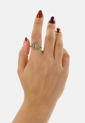 Anello in oro e argento con design della fascia intrecciata e una pietra ovale centrale, mostrato su una mano con unghie curate.