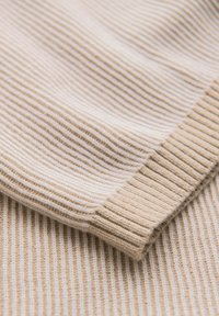 Gros plan sur un tissu en maille côtelée beige montrant un revers de manche plié avec des lignes texturées verticales.