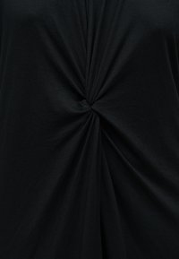 Μαύρο ύφασμα στριμμένο σε κεντρικό κόμπο δημιουργώντας ακτινικές πτυχώσεις και υφή στην επιφάνεια.