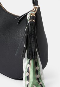 Czarna torebka skórzana z fakturą, z złotym zamkiem błyskawicznym, ozdobiona teksturowanym frędzlem i zielonym jedwabnym szalem w wzór.