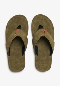 Chanclas verde oliva hechas de un material suave similar al ante, con acentos negros y costuras blancas. Presentan un plantillaje texturizado y un detalle de logo.