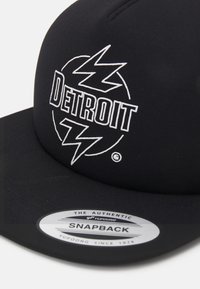 Black snapback cap featuring a white "Detroit" logo and lightning bolt design. Textured fabric with a curved visor and adjustable fit.