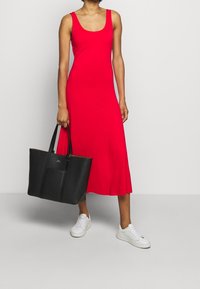 Czerwona bezrękawnik midi w elastycznym materiale zestawiona z czarną skórzaną torbą na ramię i białymi trampkami, prezentująca gładką teksturę oraz prosty design.