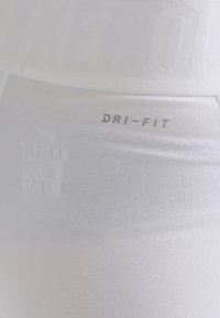 Leggings blancos Dri-Fit con textura suave, que presentan una cinturilla con marca y un detalle de logo sutil en gris claro.
