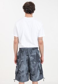 Bermuda mimetica grigia con vita elastica e cordoncino. Presenta tasche laterali e una texture di tessuto liscia e leggera.