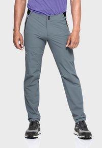 Graue Outdoor-Hosen aus leichtem Material, mit schmaler Passform, zwei Reißverschlusstaschen und Knopfverschluss, getragen mit schwarzen Sportschuhen.