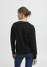 Schwarzer Sweater mit lässiger Passform, abgesenkten Schultern und gerippten Bündchen, kombiniert mit eng anliegenden blauen Jeans. Weiche Textur, minimales Design.