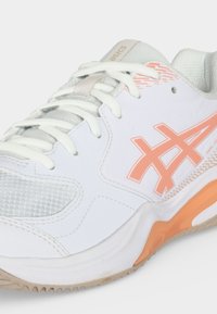 Άσπρα και μπεζ αθλητικά παπούτσια Asics με ροδακινί λεπτομέρειες, τμήματα από διχτυωτό ύφασμα και λευκά κορδόνια.