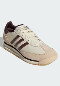 Teniska Adidas SL 72 v krémové a hnědé barvě. Vyrobená z semiše a kůže, s třemi hnědými pruhy, strukturovaným jazykem a tlustou gumovou podrážkou.