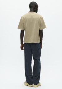 T-shirt in cotone beige con maniche corte e vestibilità rilassata, abbinato a pantaloni larghi blu scuro con due tasche posteriori e un piccolo logo.