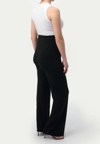 Höga svarta vida byxor i mjuk tyg, med en jämn textur och en detalj vid midjan, bärs tillsammans med en vit tanktop.