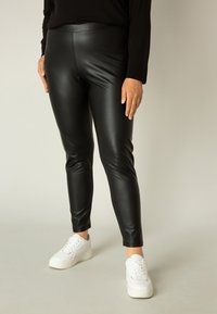 Zwarte nepleer leggings met een strakke pasvorm en een gladde textuur, gecombineerd met witte sneakers voor een contrasterende uitstraling.