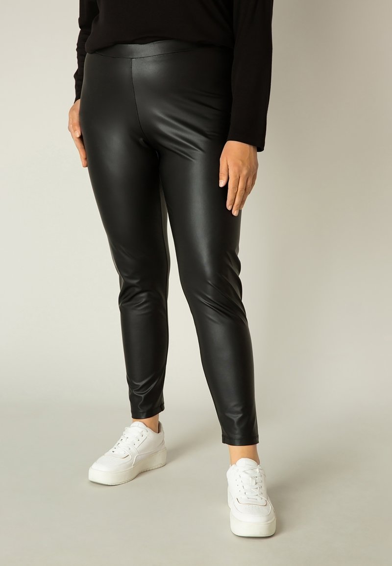 Zwarte nepleer leggings met een strakke pasvorm en een gladde textuur, gecombineerd met witte sneakers voor een contrasterende uitstraling.