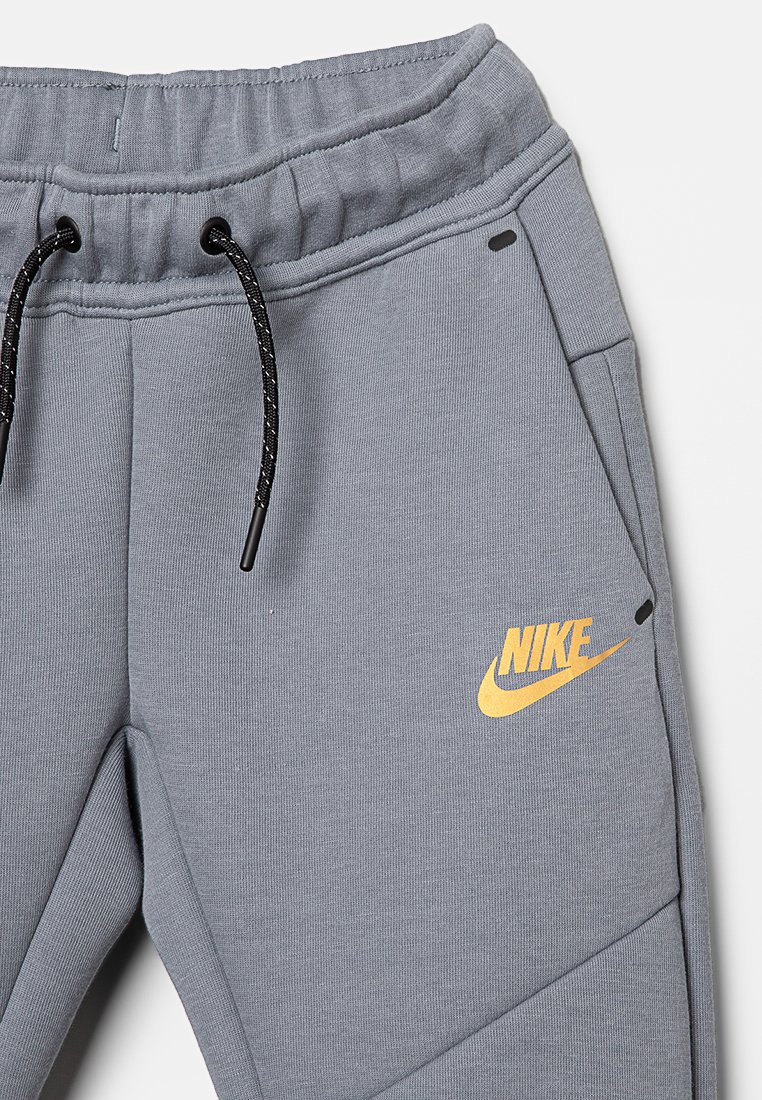 Pantaloni sportivi grigi realizzati in tessuto morbido, con un laccio nero, tasche laterali e un logo Nike giallo sulla parte inferiore della gamba sinistra.